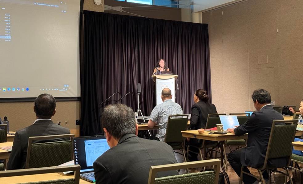 A group of people sitting at tables with laptops and a person standing at a podium Description automatically generated A group of people sitting at tables with laptops and a person standing at a podium Description automatically generated